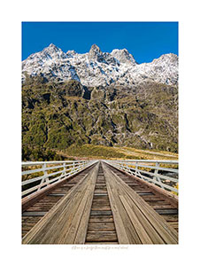 Composite of old wooden bridge and snow-capped mountains at rear; Button for Bridge Gallery.